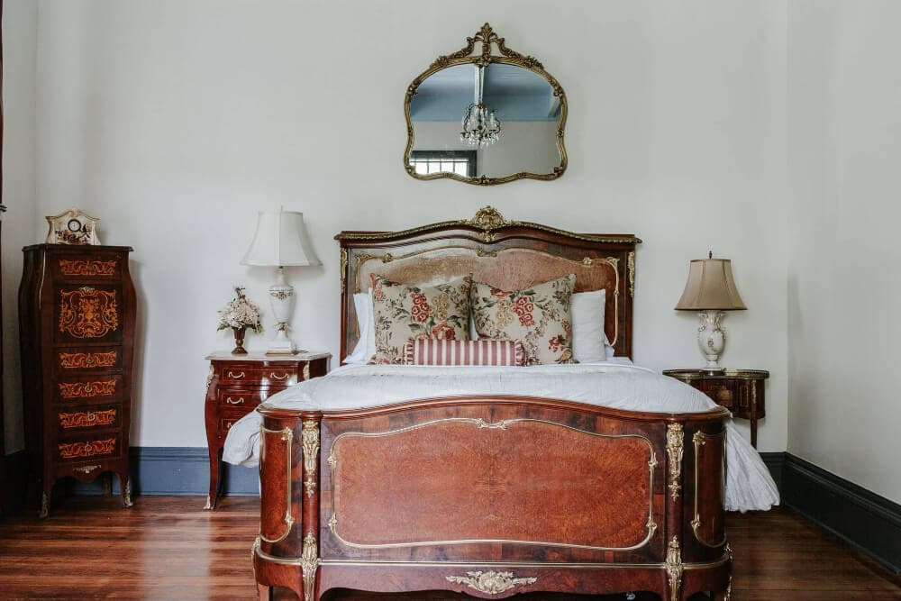 A vintage-style bedroom featuring a carved wooden bed, elegant lamps, and ornate mirror.